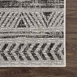 Close-up of the Catrine Indoor & Outdoor Rug. Bohemian style rug in black, charcoal, and off-white colors on dark wood floor. Swatch