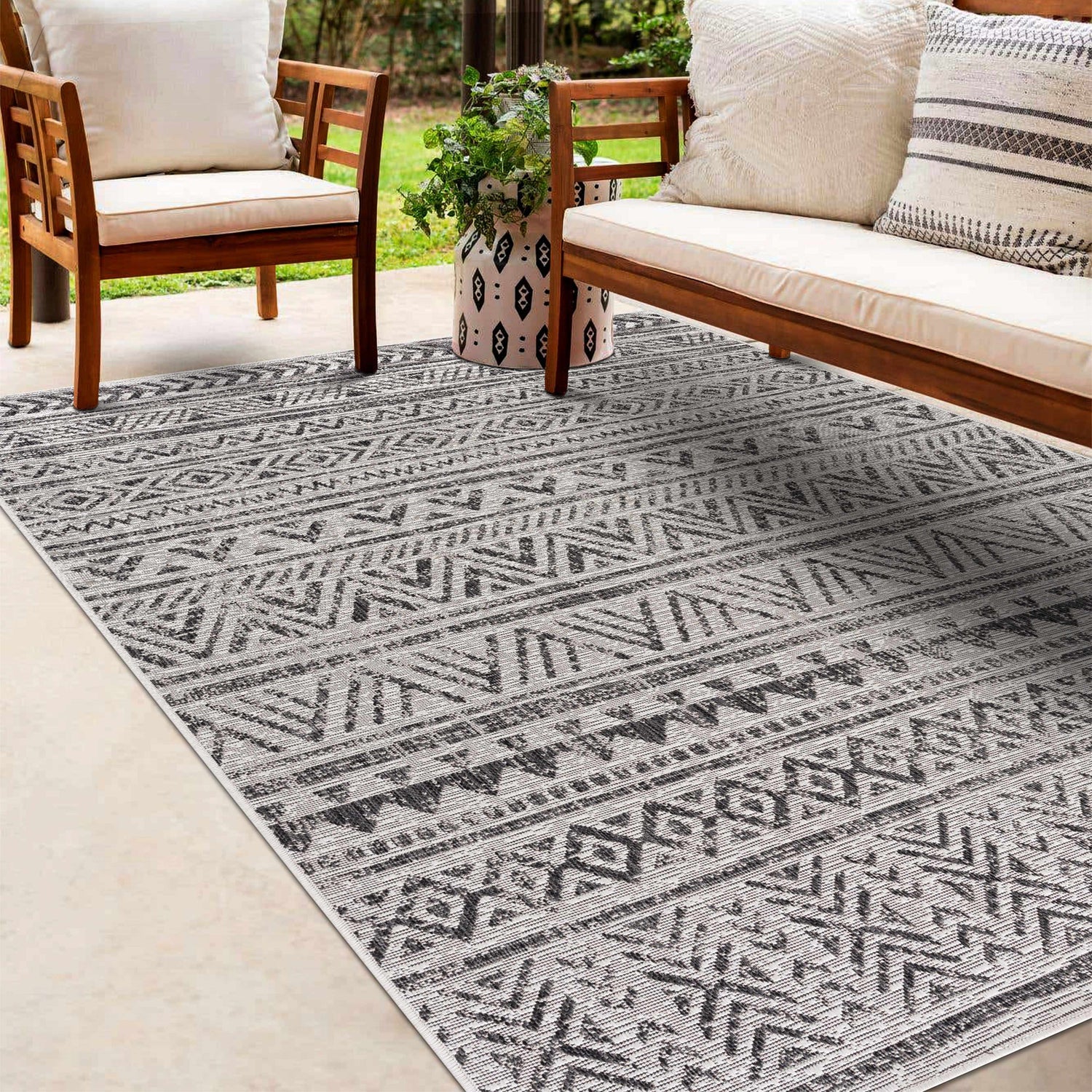 Outdoor patio scene with a black and white geometric Catrine Indoor & Outdoor Rug, wooden furniture, and neutral cushions. Roomscene-Rectangle