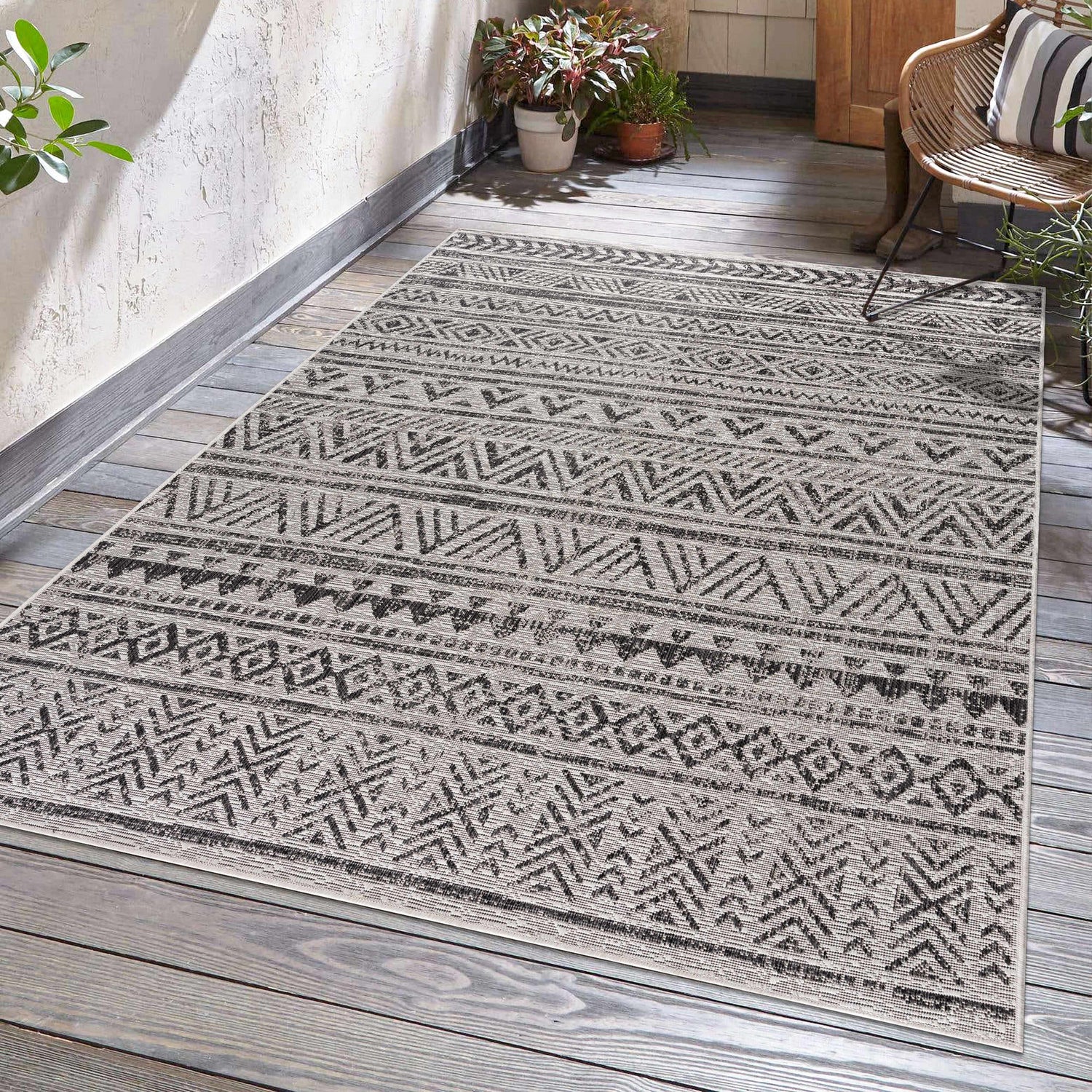 Outdoor patio scene with a black and white geometric Catrine Indoor & Outdoor Rug on gray wood planks. Roomscene-Rectangle