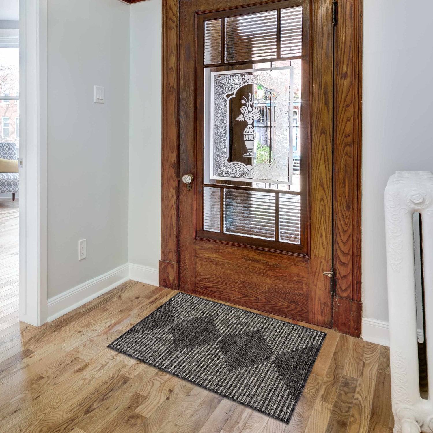 Entryway scene with a Stephan Area Rug in black, charcoal, cream, and light gray colors, wooden door with glass, and hardwood floor. Roomscene-Rectangle