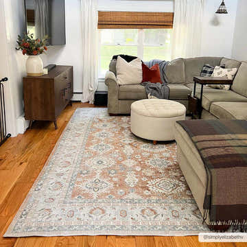 Living room scene with Ezio Boutique Washable Rug in rust, light blue, and off-white under a gray couch and ottoman. Roomscene-Rectangle