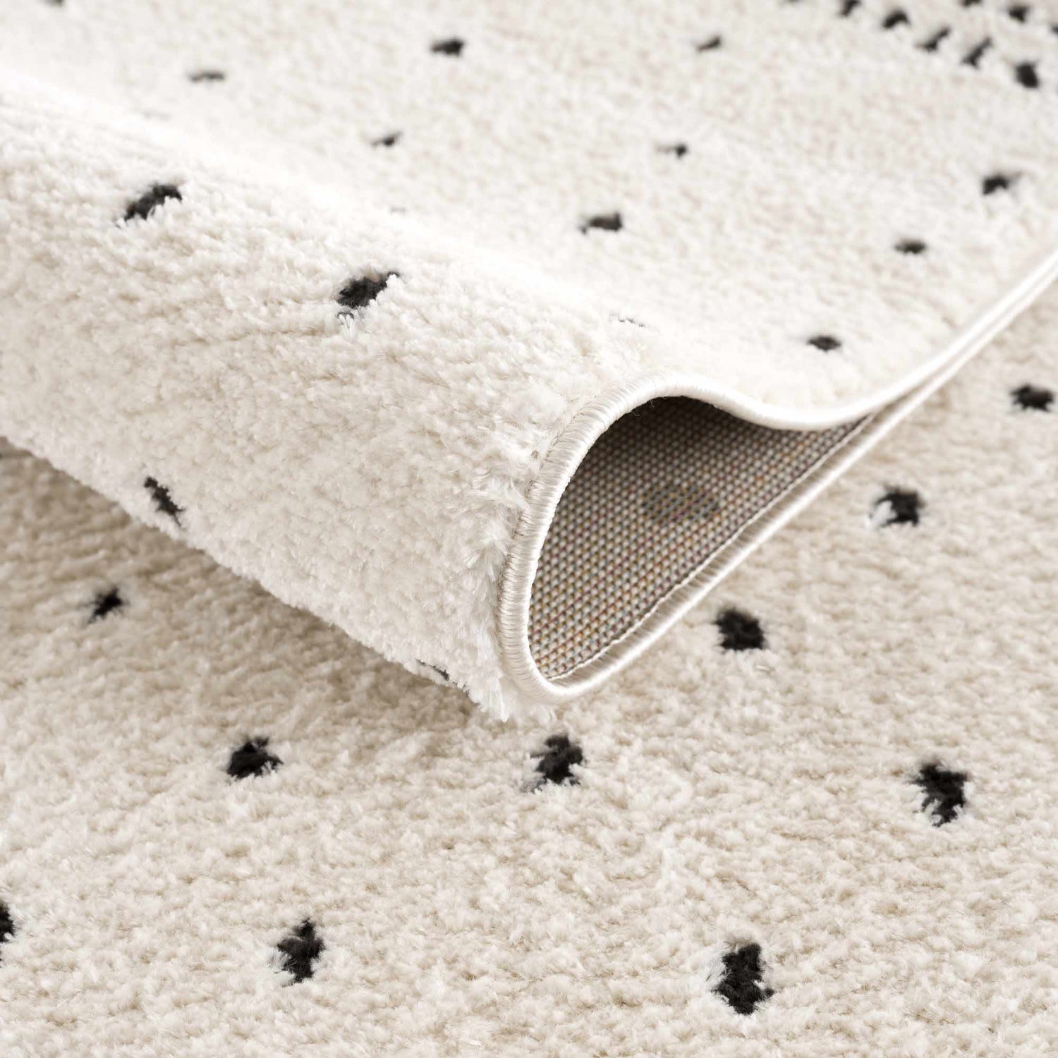 Close up of the Julie Area Rug showing its beige, fluffy texture and black polka dot geometric pattern. Fold