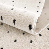 Close-up of the Julie Area Rug showing its beige, plush texture and black polka dot geometric pattern. Fold