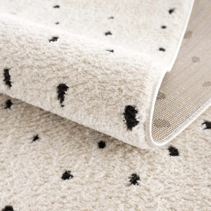 Close-up of the Julie Area Rug showing its beige, plush texture and black polka dot geometric pattern. Fold