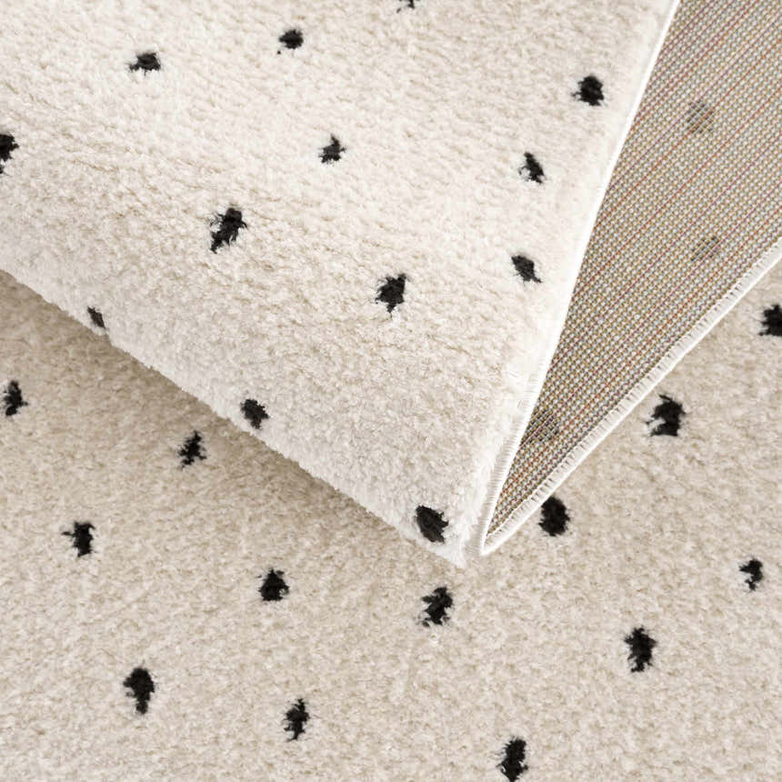 Close-up of the Julie Area Rug. Beige rug with black polka dot pattern and soft, textured pile. Fold