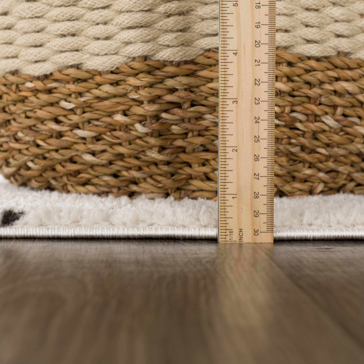Close-up of Julie area rug pile height. Beige and ivory geometric pattern. Ruler shows rug thickness. Pile