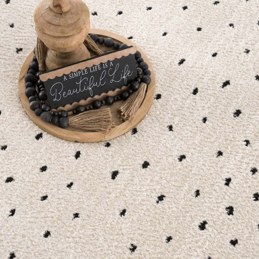 Close-up of the Julie Area Rug, a beige rug with a black polka dot pattern and textured, machine woven construction. Styleshot