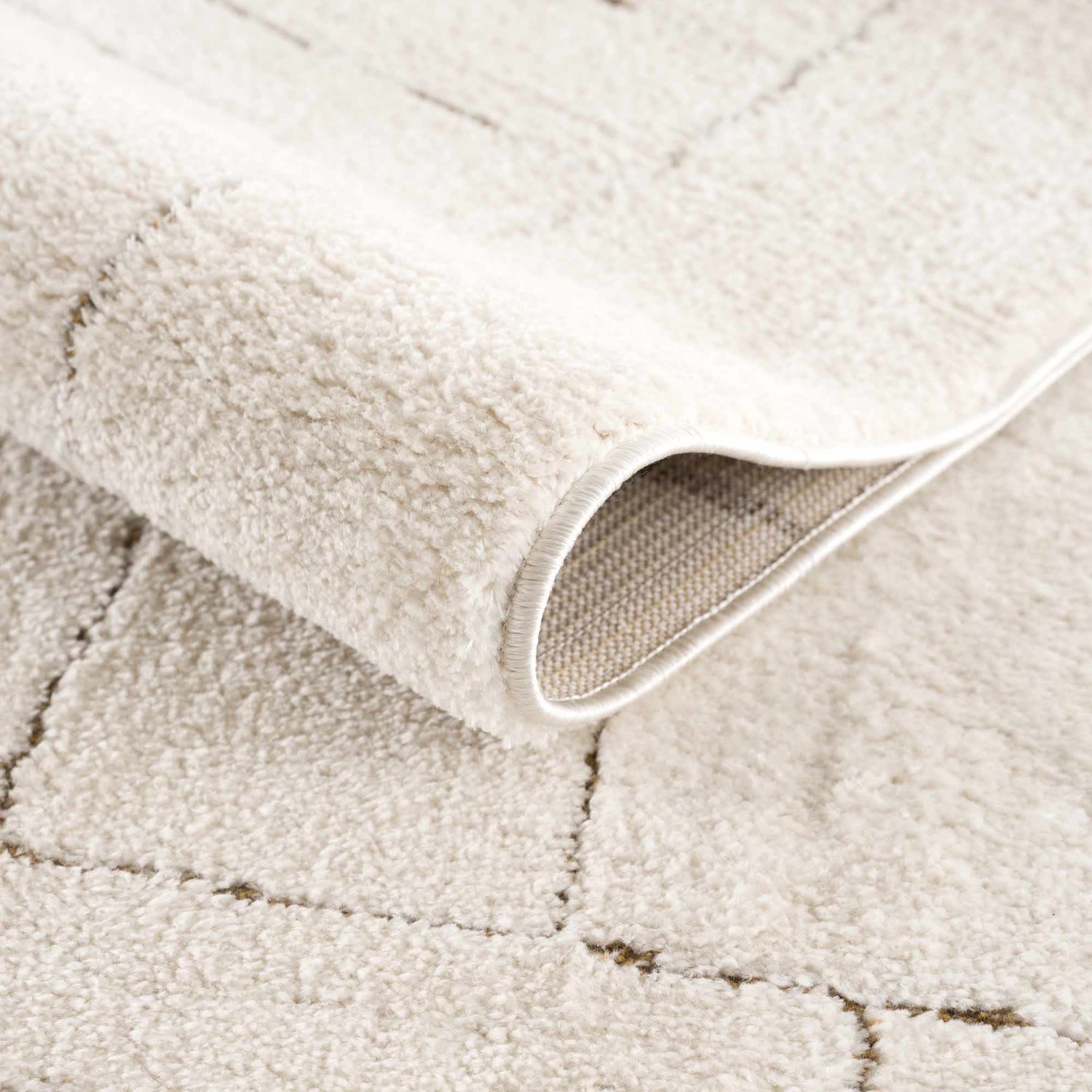 Close-up of the Keats Area Rug showing its plush ivory pile, brown geometric pattern, and durable machine-woven construction. Fold
