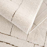 Close-up of the Keats Area Rug showing its plush beige pile, brown geometric pattern, and durable machine-woven construction. Fold