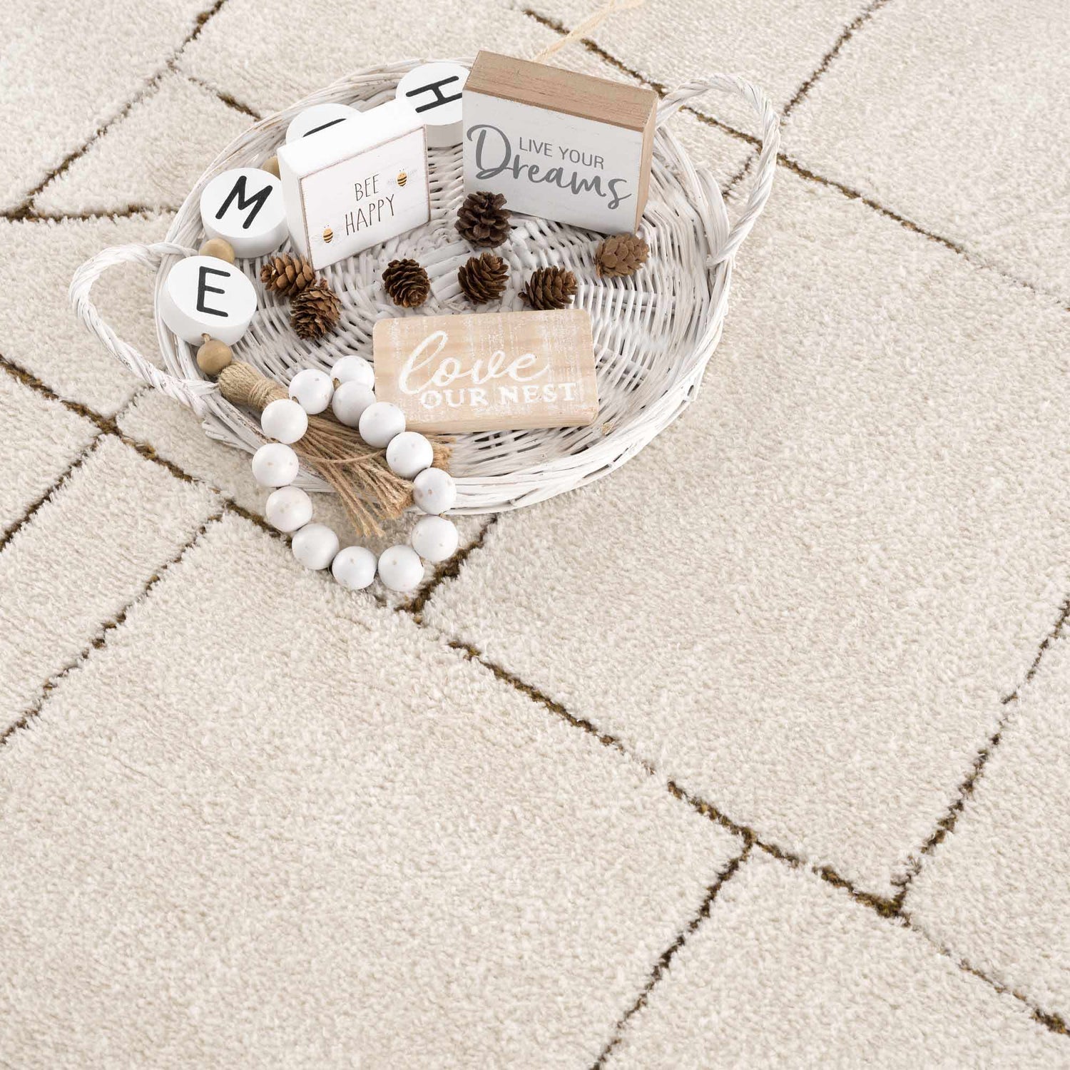 Close-up of the Keats Area Rug's beige shag texture and brown geometric line pattern. White decor basket with pinecones. Styleshot