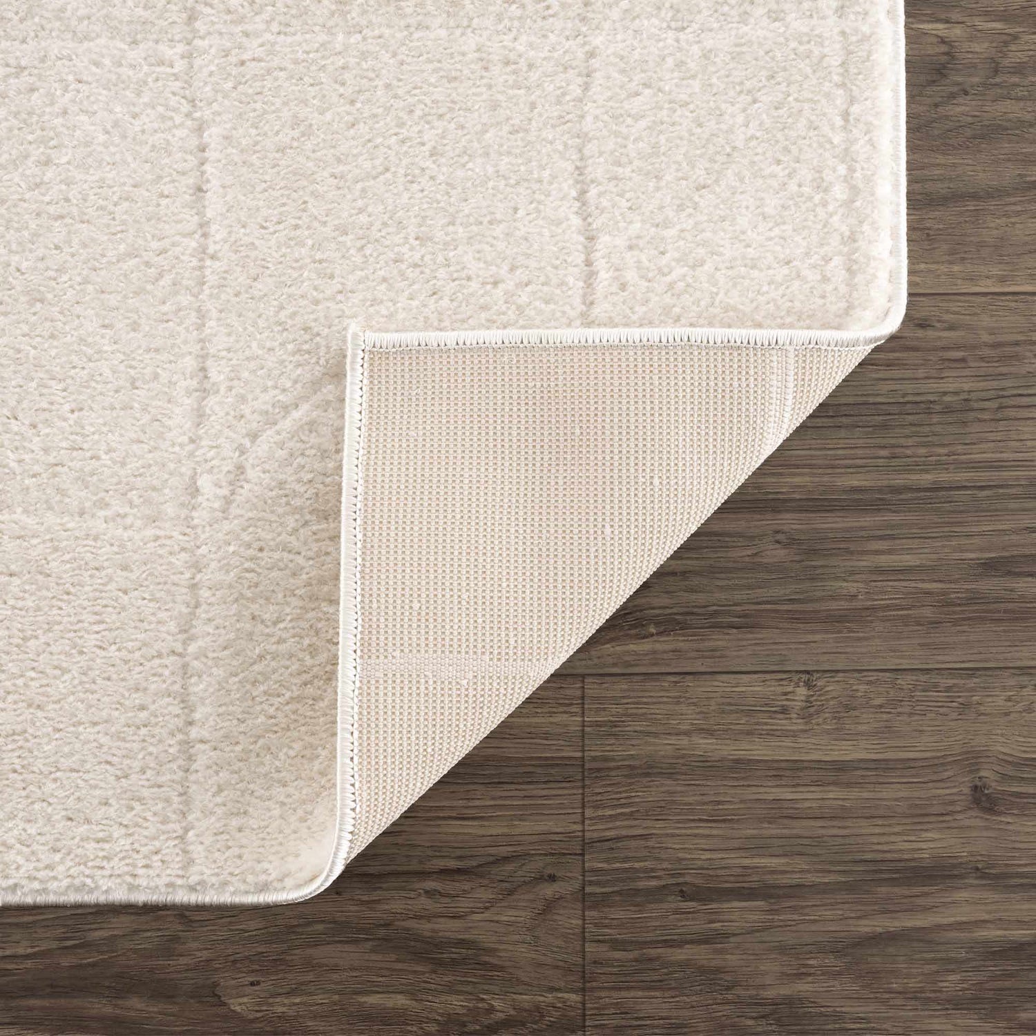 Close-up of the ivory Keanu Area Rug showing its plush texture, backing, and edge on dark wood flooring. Fold