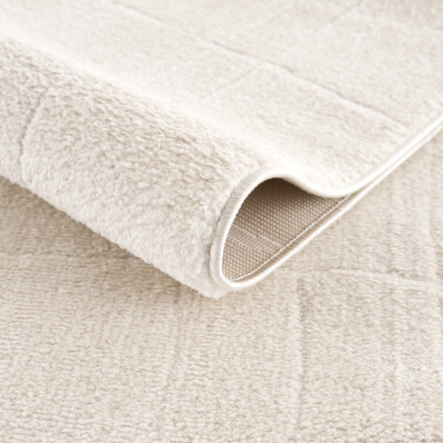 Close-up of the plush, ivory Keanu Area Rug showing its soft texture, backing, and subtle geometric pattern. Fold