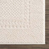 Close-up of the ivory Julio Area Rug showing its plush texture and subtle geometric pattern on dark wood flooring. Swatch