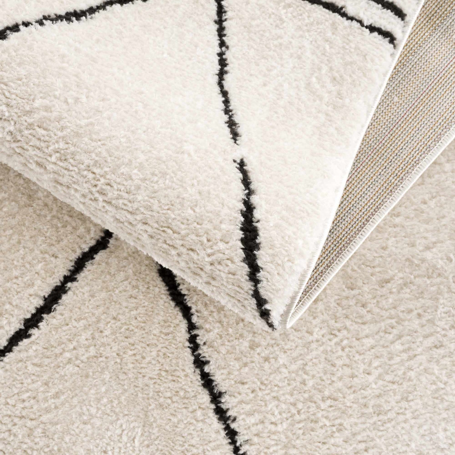 Close-up of the Keone Black & White rug showing its plush texture and black geometric line pattern on a beige background. Fold