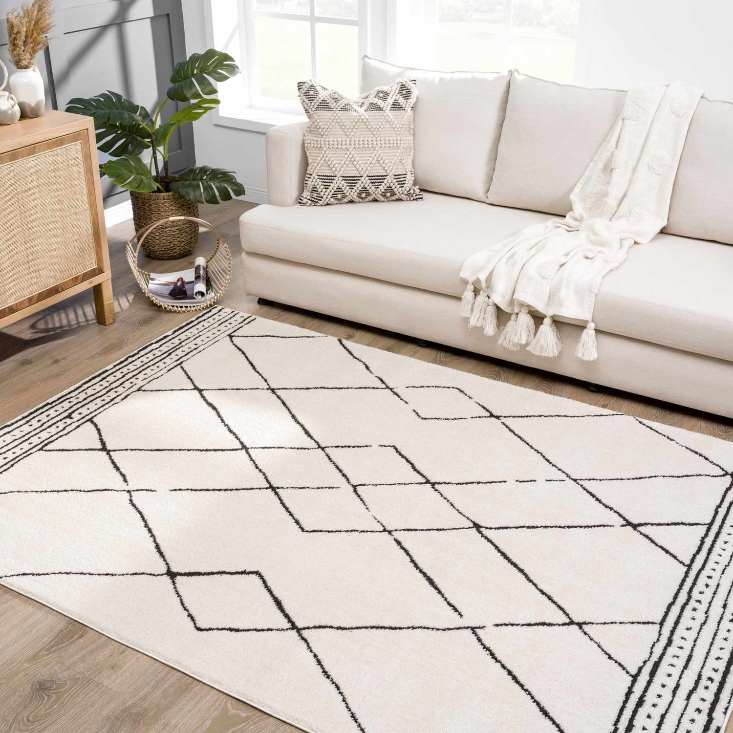 Living room scene with a Keone Black & White rug, beige sofa, wood cabinet, and monstera plant. Roomscene-Rectangle