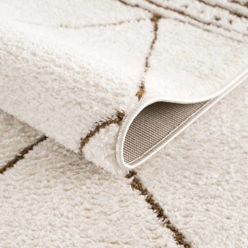 Close-up of the plush, ivory Keone Area Rug with a geometric brown pattern and rolled edge showing the backing. Fold