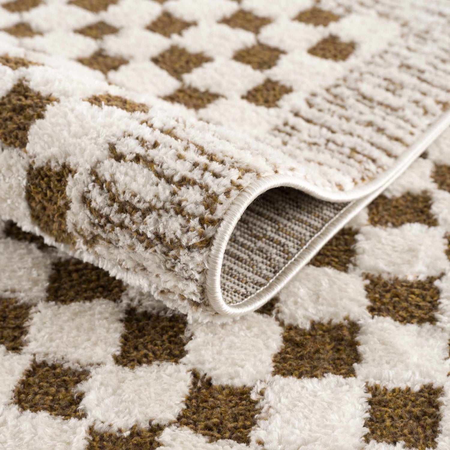 Close-up of Leryn Brown Checkered Plush Rug showing its soft texture, brown and ivory checkered pattern, and machine-woven construction. Fold