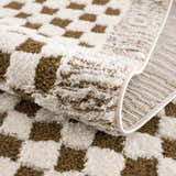 Close up of the Leryn Brown Checkered Plush Rug showing its plush texture and brown and ivory geometric pattern. Fold