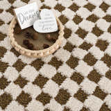 Close-up of the Leryn Brown Checkered Plush Rug, featuring a geometric brown and ivory checkerboard pattern and soft texture. Styleshot