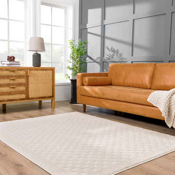 Living room scene with a Leryn Ivory Checkered Area Rug, tan leather sofa, wood cabinet, and gray accent wall. Roomscene-Rectangle