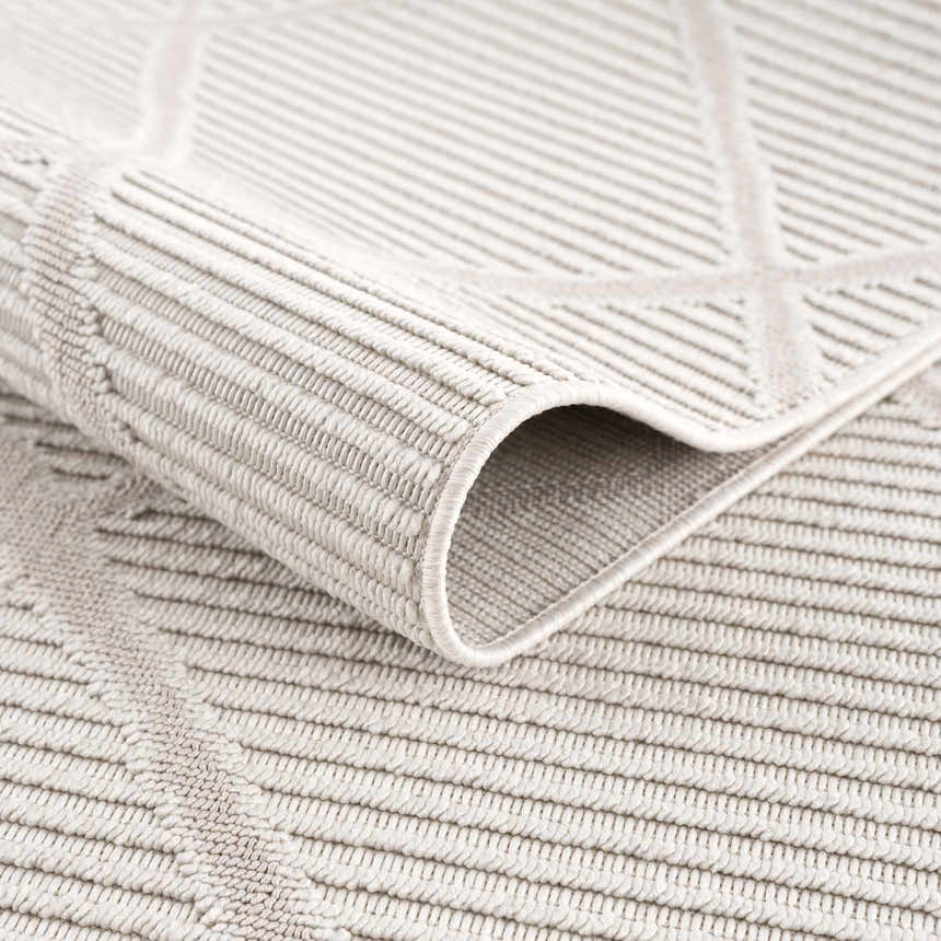 Close-up of the beige Lova Area Rug showing geometric pattern and textured, machine-woven construction. Fold
