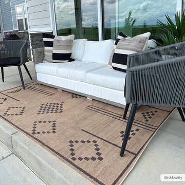 Outdoor patio scene with a camel Fathi Washable Area Rug, white sofa, and gray chairs. The rug has a geometric dark brown pattern. Roomscene-Rectangle