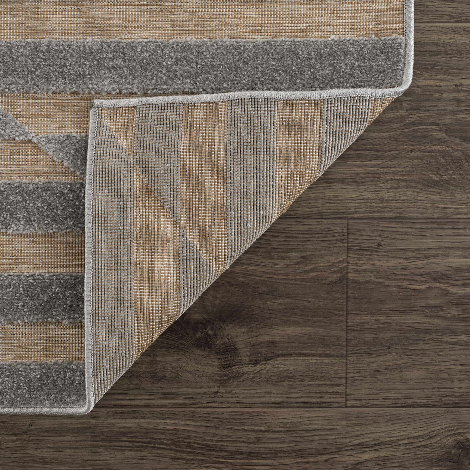 Close-up of the Webuye 3D Outdoor Area Rug showing gray geometric pattern and woven backing on dark wood floor. Fold