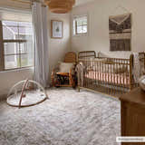 Light and airy nursery with a vintage-style Gael Boutique Washable Rug, gold crib, and wooden rocking chair. Roomscene-Rectangle