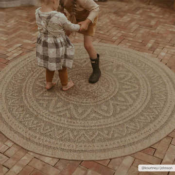 Kids playing on a round Gitel Area Rug in a brick patio setting. The rug is beige with a traditional pattern. Roomscene-Round