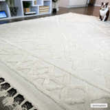Close-up of the bone-colored Gyundyukoru Area Rug, a geometric design with tassels, on a dark wood floor. Roomscene-Rectangle