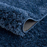 Close-up of the plush texture of the Faina Solid Dark Blue Shag Washable Area Rug, showing the backing. Fold