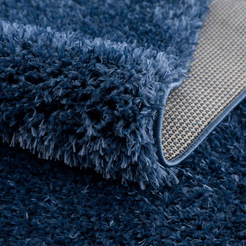 Close-up of the plush texture and backing of the Faina Solid Dark Blue Shag Washable Area Rug. Fold