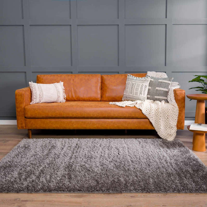 Living room scene with a Faina Solid Dark Gray Shag Washable Area Rug, tan leather sofa, and gray accent wall. Roomscene-Rectangle