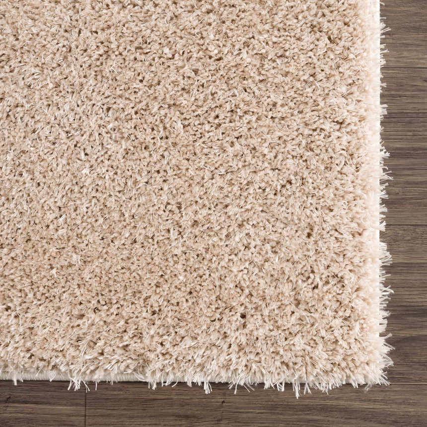 Close-up of the plush texture of the Faina Solid Beige Shag Washable Area Rug on dark wood flooring. Swatch