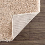 Close-up of the Faina Solid Beige Shag Washable Area Rug showing its plush texture and durable backing on a wood floor. Fold