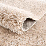 Close-up of the plush texture of the Faina Solid Beige Shag Washable Area Rug, showing the backing. Fold