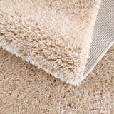 Close up of the plush texture and backing of the Faina Solid Beige Shag Washable Area Rug. Fold