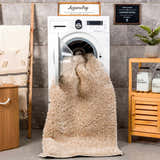 Laundry room scene with Faina Solid Beige Shag rug emerging from washing machine. Modern decor with wood accents and gray tile. Washing-Machine