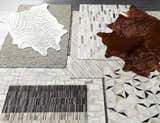 Close-up of several Wauzeka Premium Area Rugs showing animal hide, geometric, and striped designs in brown, cream, and gray tones. Styleshot