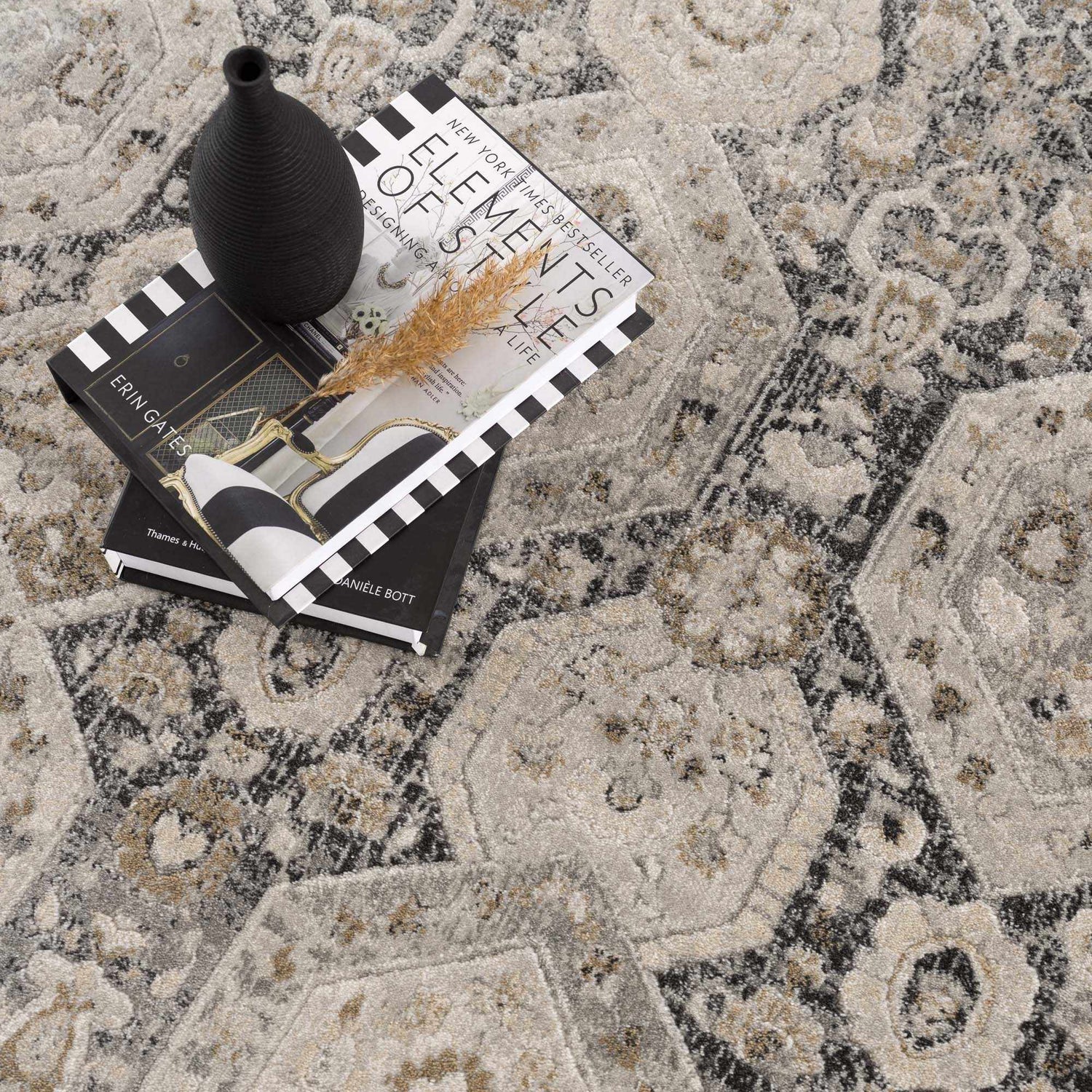 Close-up of the Minoa Area Rug featuring a beige, black, and gray bohemian pattern. Styled with books and a black vase. Styleshot