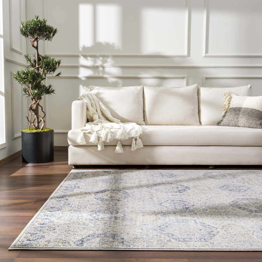 Living room with cream sofa, tree, and Parkerfield Cream & Blue Area Rug on dark wood floor. Sunlight streaming through window. Roomscene-Rectangle