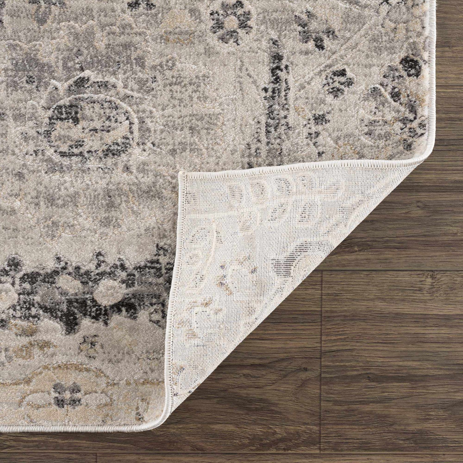 Close-up of Georgiana Area Rug showing beige, black, and gray floral pattern and machine woven construction on wood floor. Fold