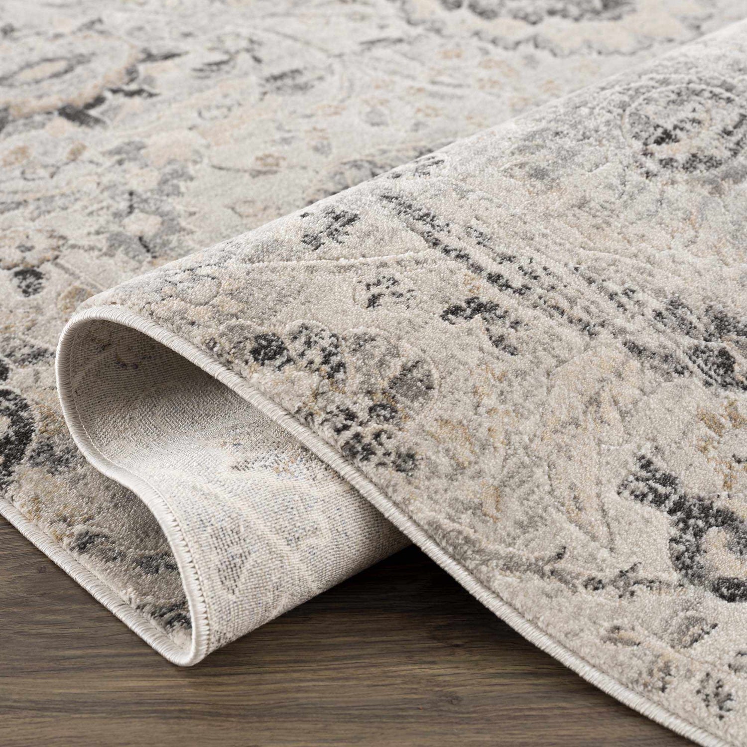 Close-up of the Georgiana Area Rug showing its beige, black, and gray floral Persian-style pattern and machine-woven texture. Fold