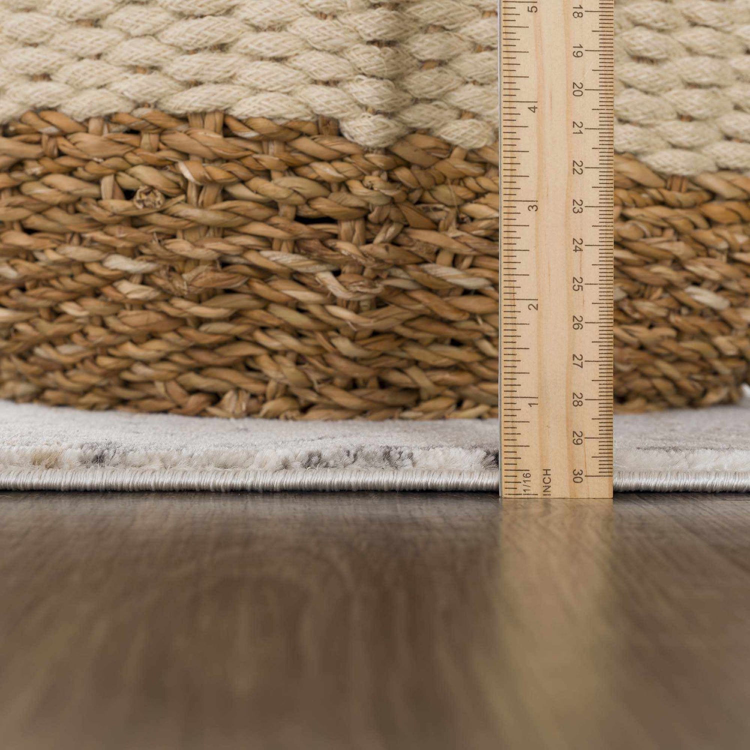 Close-up of the Georgiana Area Rug showing the pile height with a ruler and a woven basket. Beige and gray tones. Pile