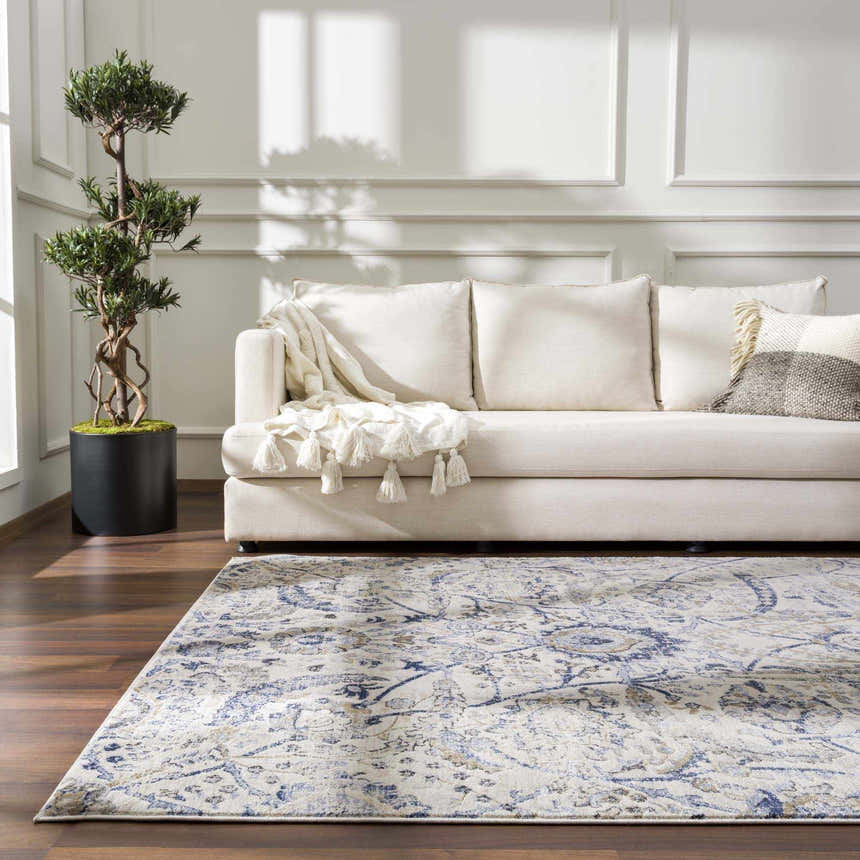 Living room scene with a Georgiana Blue & Beige Oushak Rug, cream sofa, decorative tree, and wood floors. Roomscene-Rectangle
