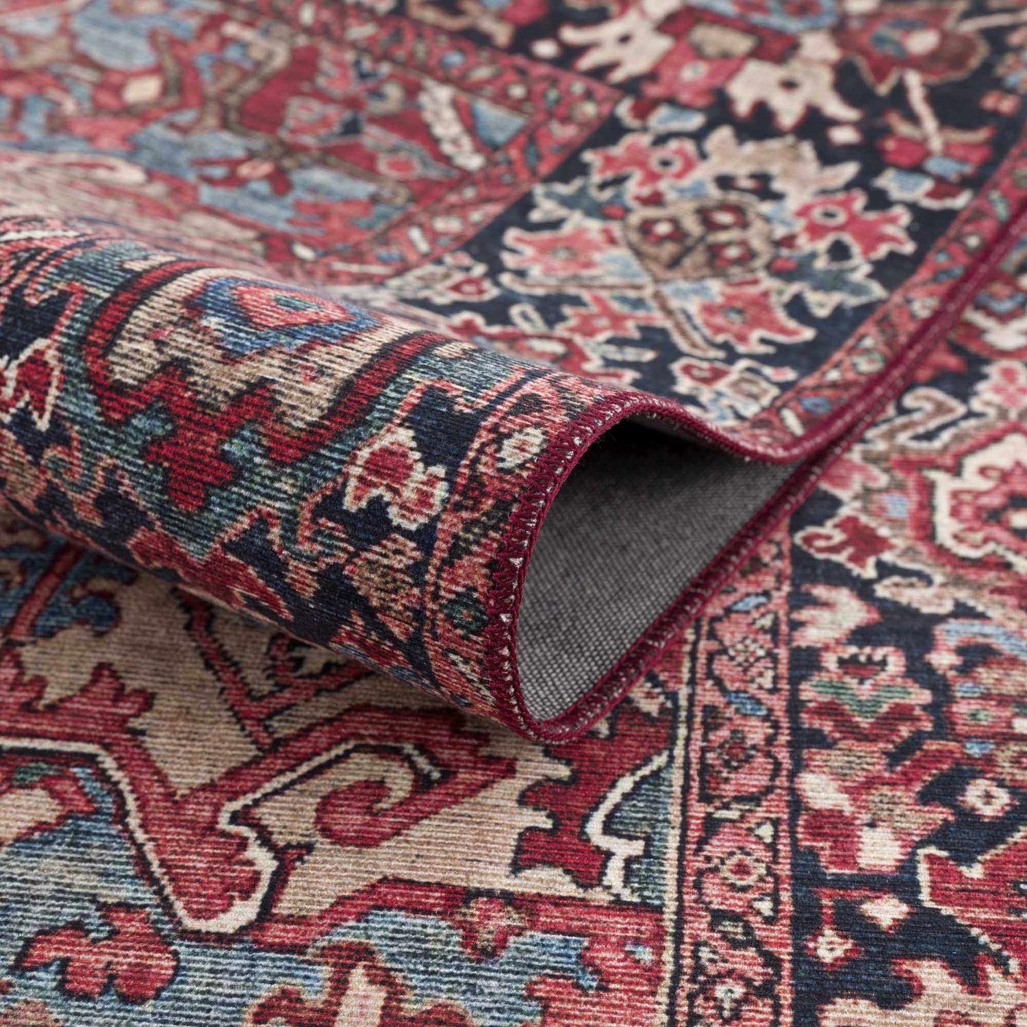 Close-up of the Neyland Area Rug, showing its traditional design, beige, red, and blue colors, and machine-woven texture. Fold