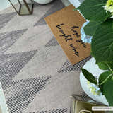 Entryway scene with a camel Ijlal Washable Area Rug, doormat, lantern, and hydrangea in a vase. Roomscene-Rectangle