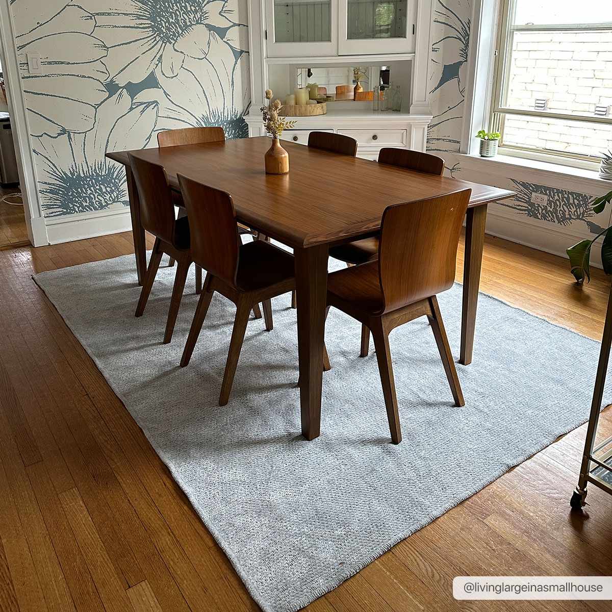 Dining room scene with wood table and Isako Light Blue Solid Washable Rug on hardwood floors, floral wallpaper. Roomscene-Rectangle