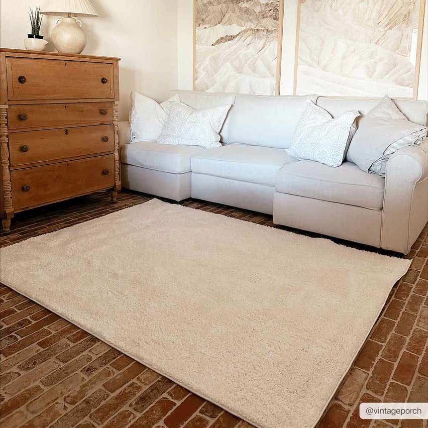 Living room scene with a Judy White Washable Area Rug, a white sofa, and a vintage wooden dresser on a brick floor. Roomscene-Rectangle