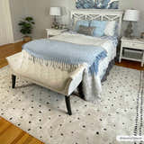 Bedroom scene with the Julie Area Rug in beige and black, beneath a bench and bed with blue accents. Roomscene-Rectangle